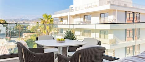 Un balcon avec une table et des chaises, un bâtiment blanc en arrière-plan et une vue sur la ville.