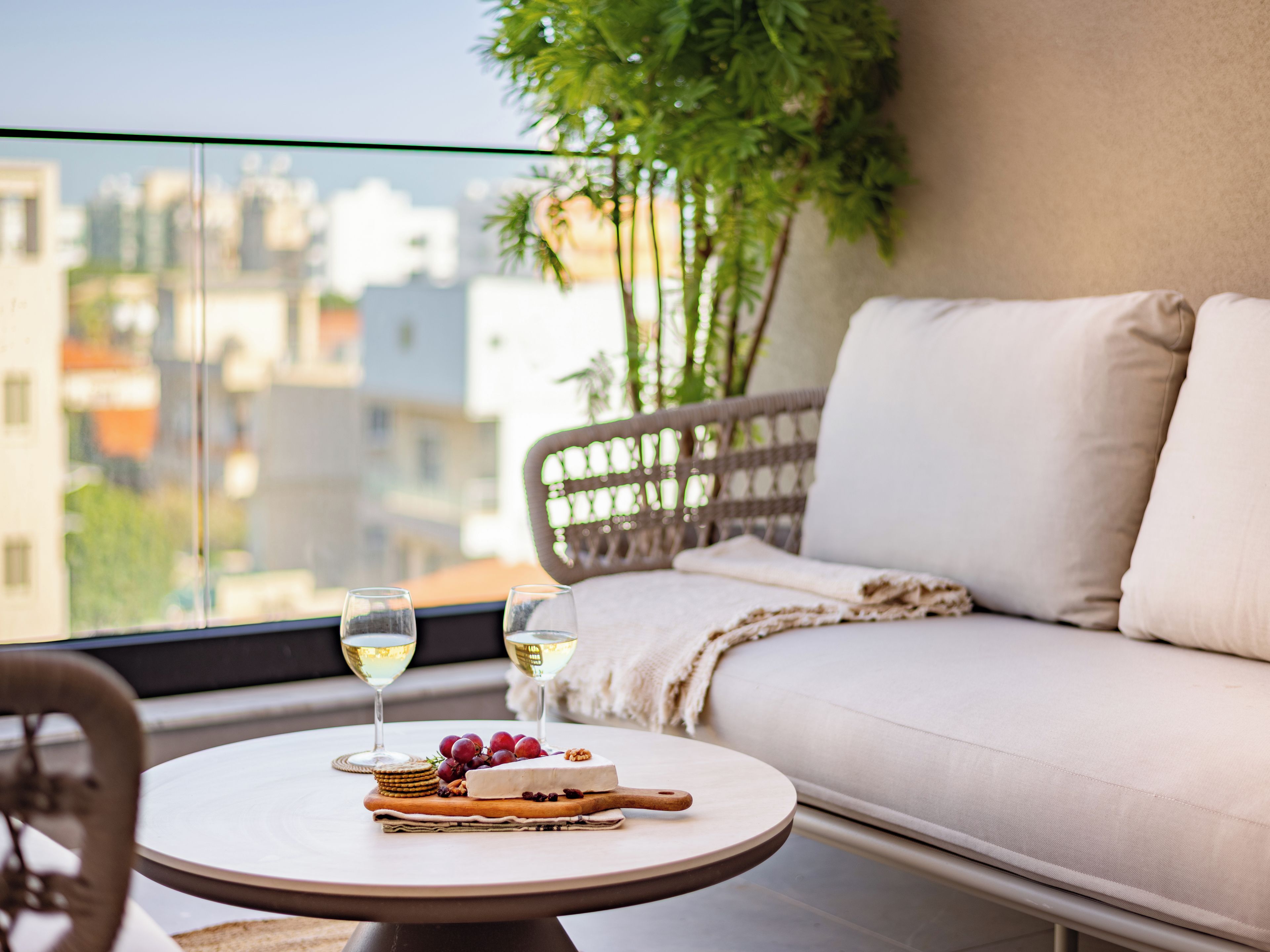 Varanda com mesa redonda, sofá de vime e vista para a cidade.