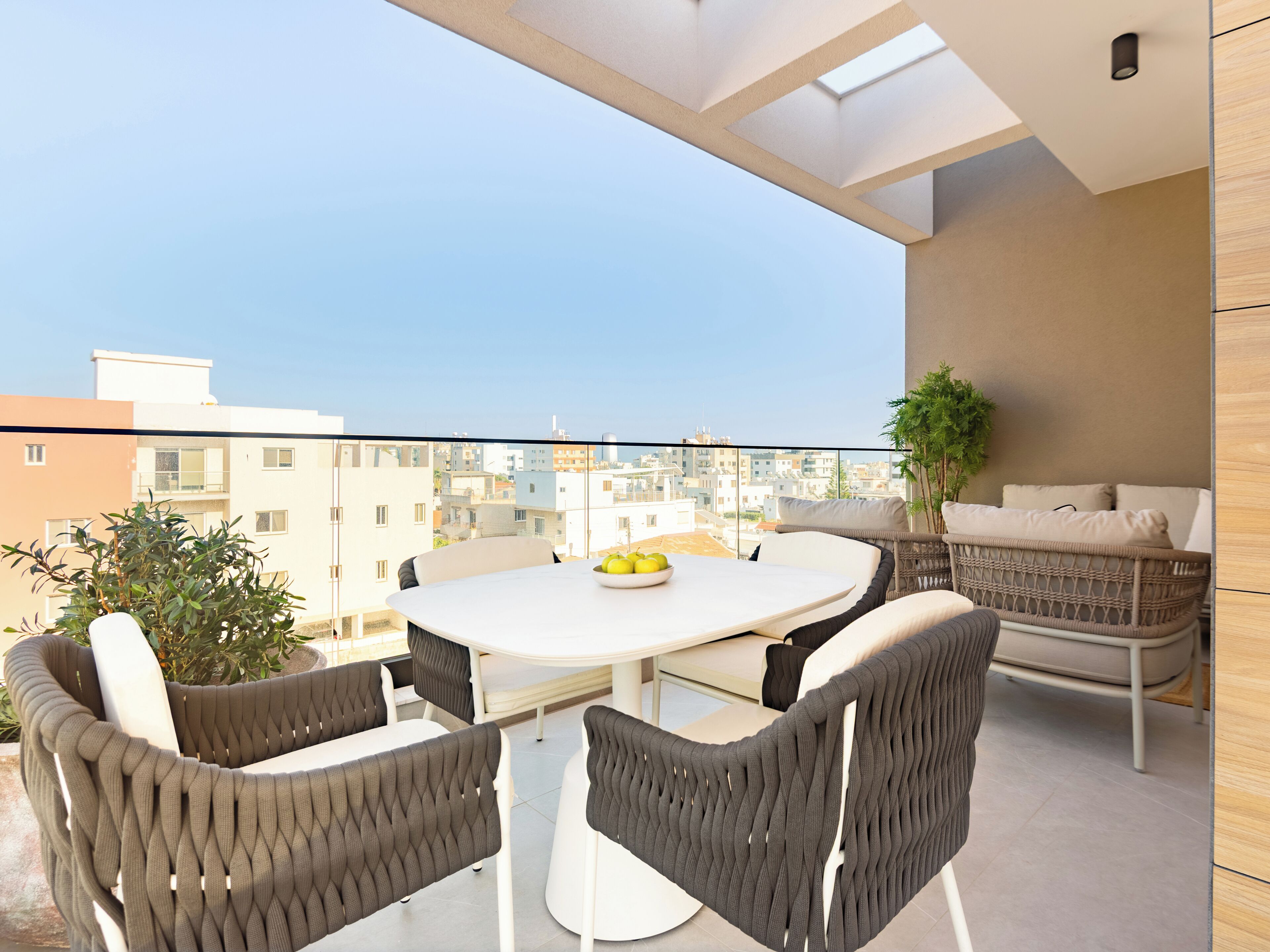 A balcony with a round table, four chairs, a potted plant, and a wicker sofa.