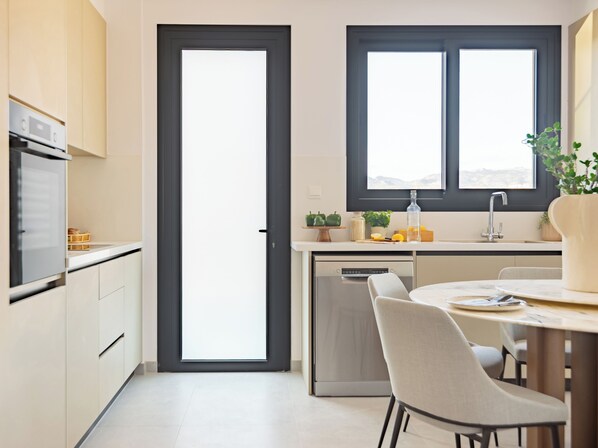A modern kitchen with a dishwasher, a dining table with chairs, a window with a view, and a door. - Sanders City Boutique - Full Building (Limassol)