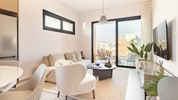 A modern living room with a sofa, chairs, a coffee table, a TV, and a balcony with plants.