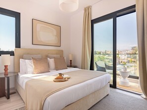 Camera d'albergo con un letto grande, un comodino con una lampada, vista sulla città attraverso un'ampia finestra e un balcone con una sedia.