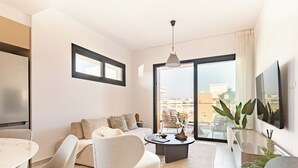 Uma sala de estar moderna com sofá, cadeiras, mesa de centro, TV e varanda com plantas.