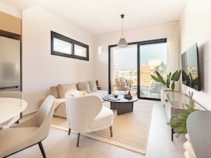 A modern living room with a sofa, chairs, a coffee table, a TV, and a balcony with plants. - Sanders City Boutique - Full Building (Limassol)