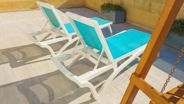 Une terrasse avec deux fauteuils blancs, dotés de coussins turquoise, une balançoire en bois et une vue sur la mer.