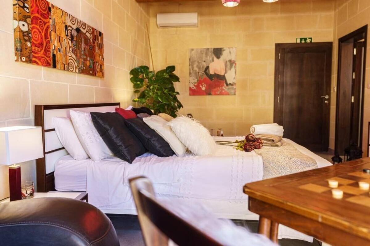 Une chambre à coucher comprenant un lit, une table de chevet, une lampe, une chaise, une table en bois avec un jeu d’échecs, une plante et des œuvres d’art accrochées aux murs.