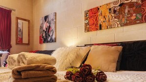 Un lit bien fait, avec une couette blanche, un oreiller blanc moelleux et une couverture beige. On peut voir des roses rouges sur le lit, ainsi qu’une pile de serviettes pliées.
