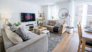 Ein modernes Wohnzimmer mit Flachbildfernseher, einer Couch, einem Couchtisch und einem Essbereich mit Tisch und Stühlen.