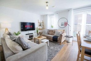 A modern living room with a flat-screen TV, a sofa, a coffee table, and a dining area with a table and chairs. - Comfortable 4 Bed Townhouse - Sleeps 9, Private Garden, Free Parking (Nottingham)