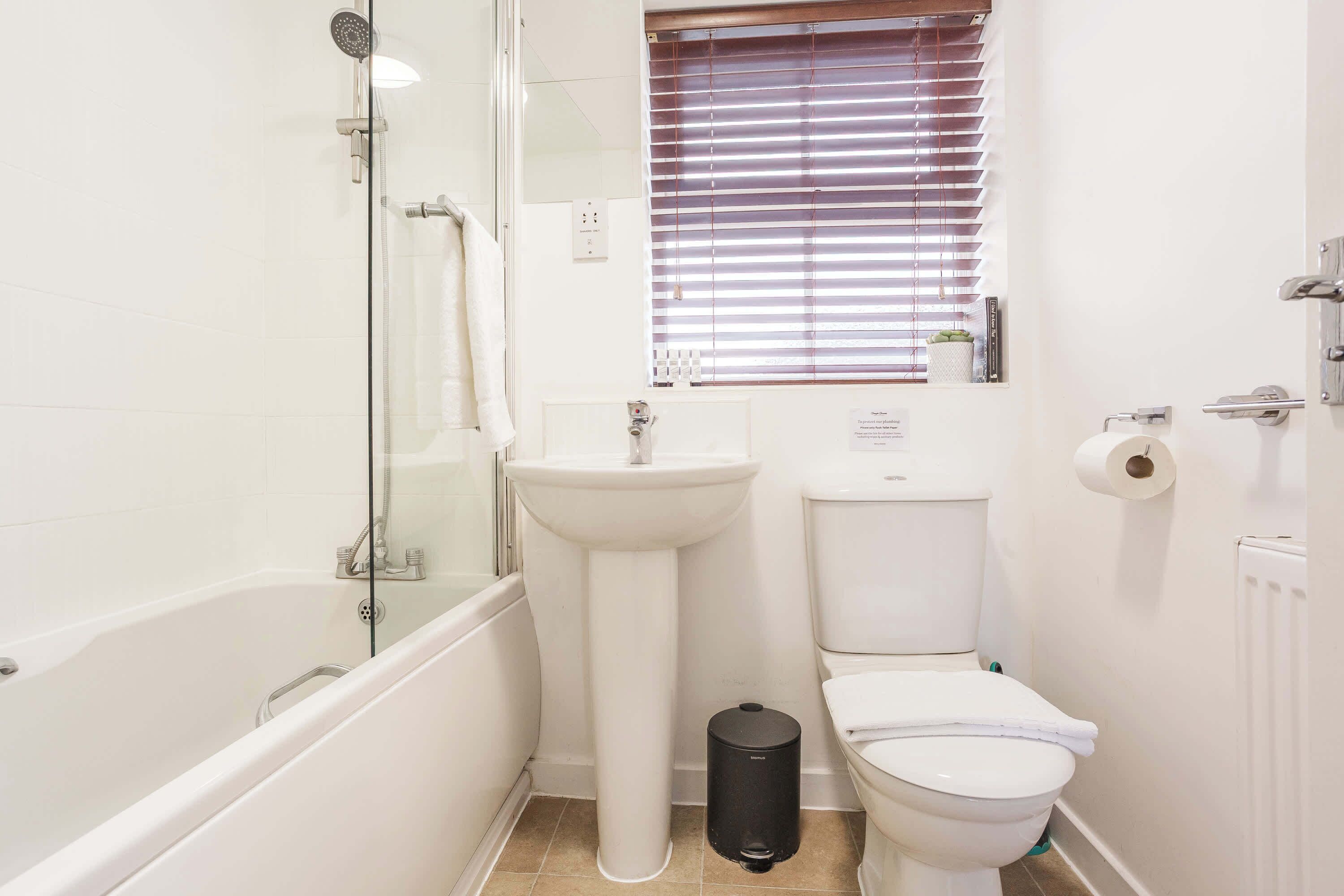 Un baño con bañera, lavabo, inodoro y una ventana con persianas.