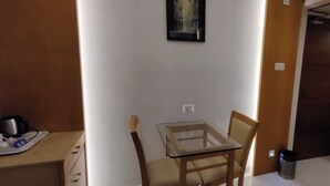 A small, well-lit room with a glass-top table, a chair, a coffee maker, and a trash can. - Hotel Mahis Gateway (Coimbatore)