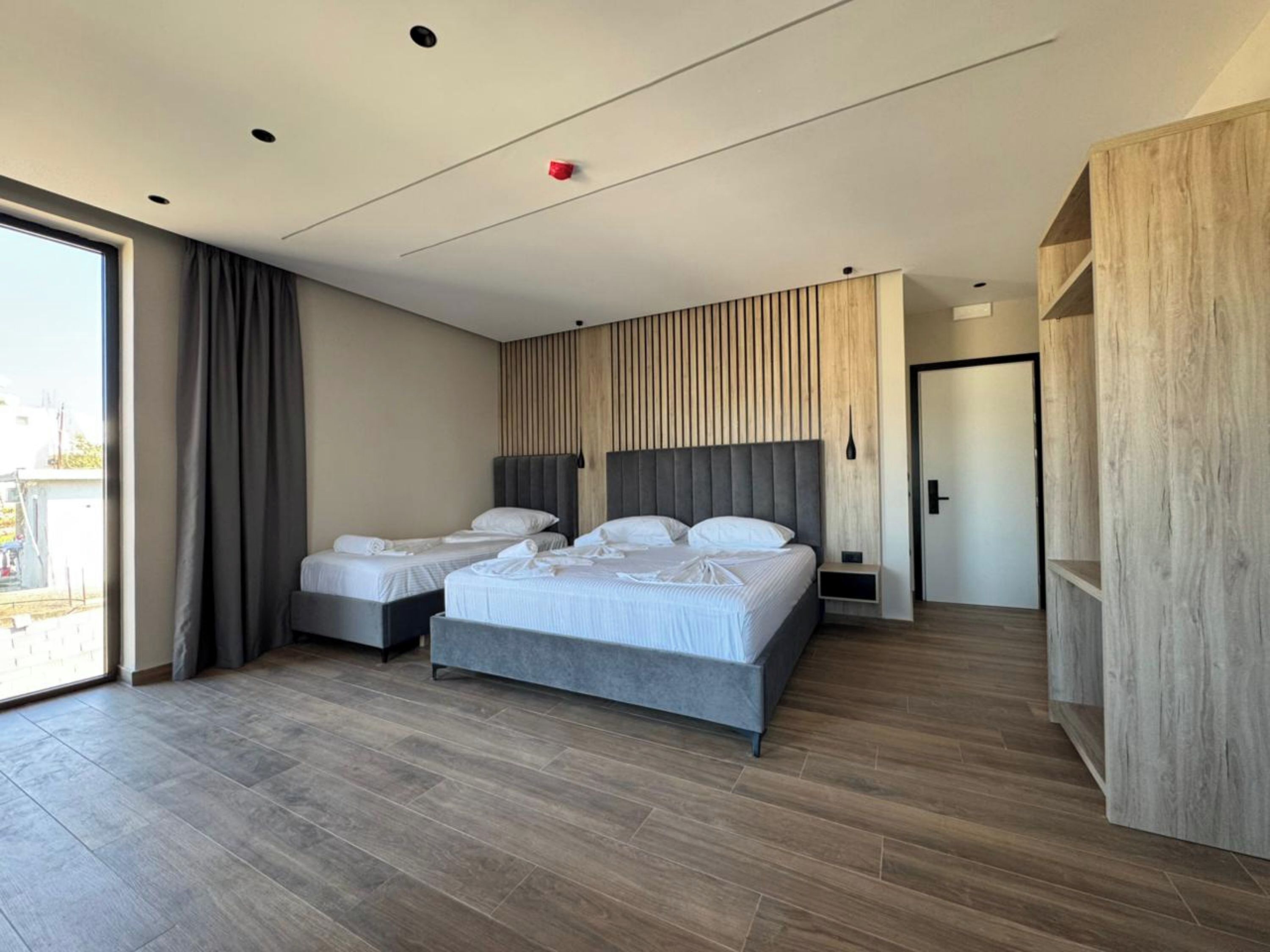 Una habitación de hotel moderna con dos camas, un ventanal amplio y una pared decorativa de madera.