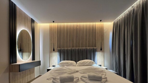 A modern bedroom with a large bed, a round mirror, and a headboard with vertical slats. - Aeris Sol Ksamil - Free Parking - Pool (Ksamil)