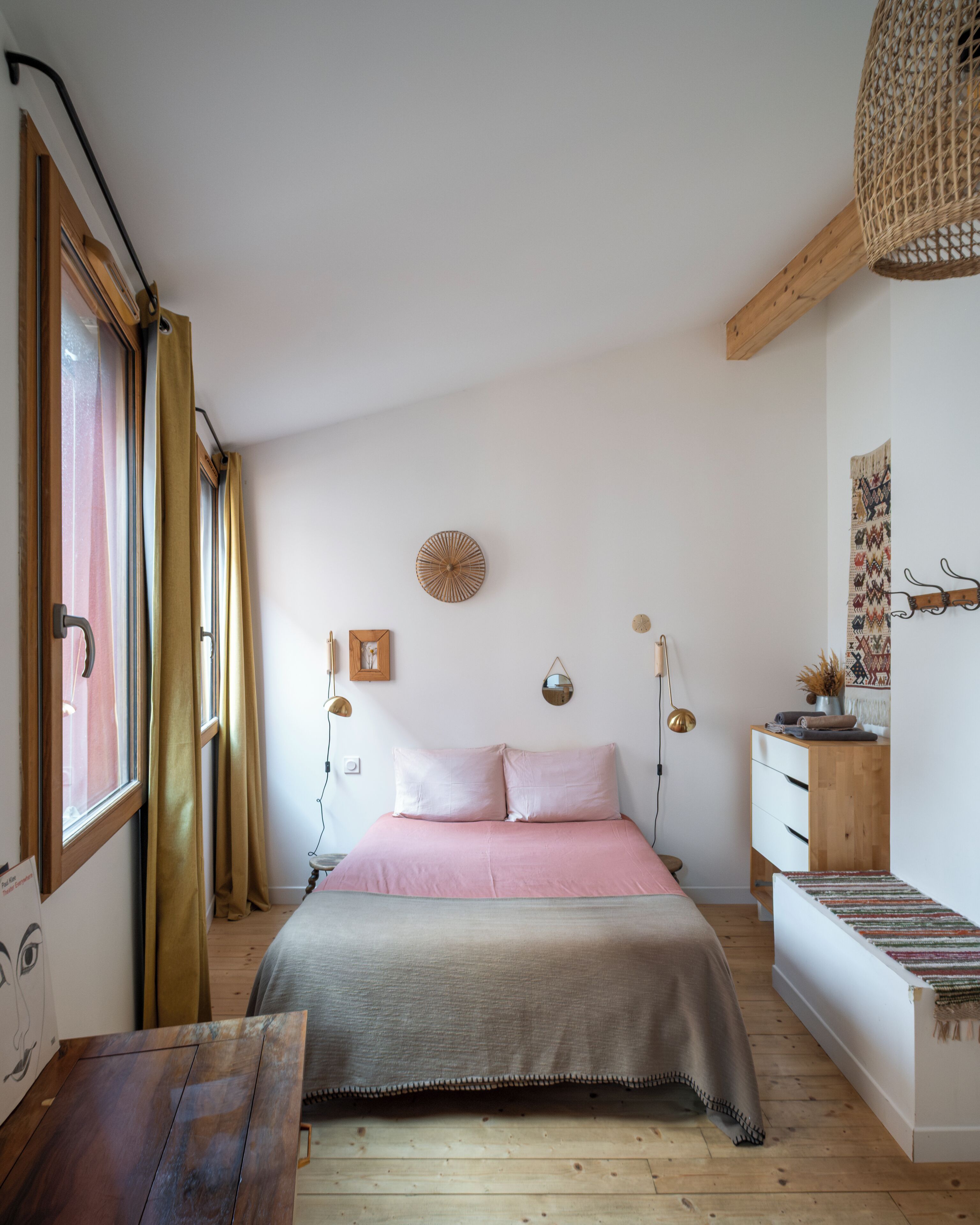 Un dormitorio con cama, suelo de madera, un escritorio, cómoda y una ventana con cortinas.
