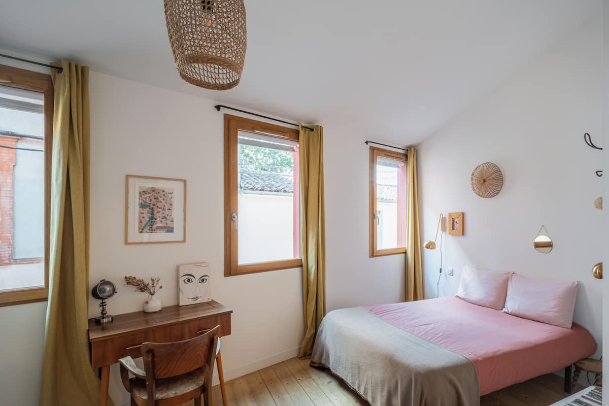 A bedroom with a wooden desk, a bed with pink bedding, and a window with curtains.