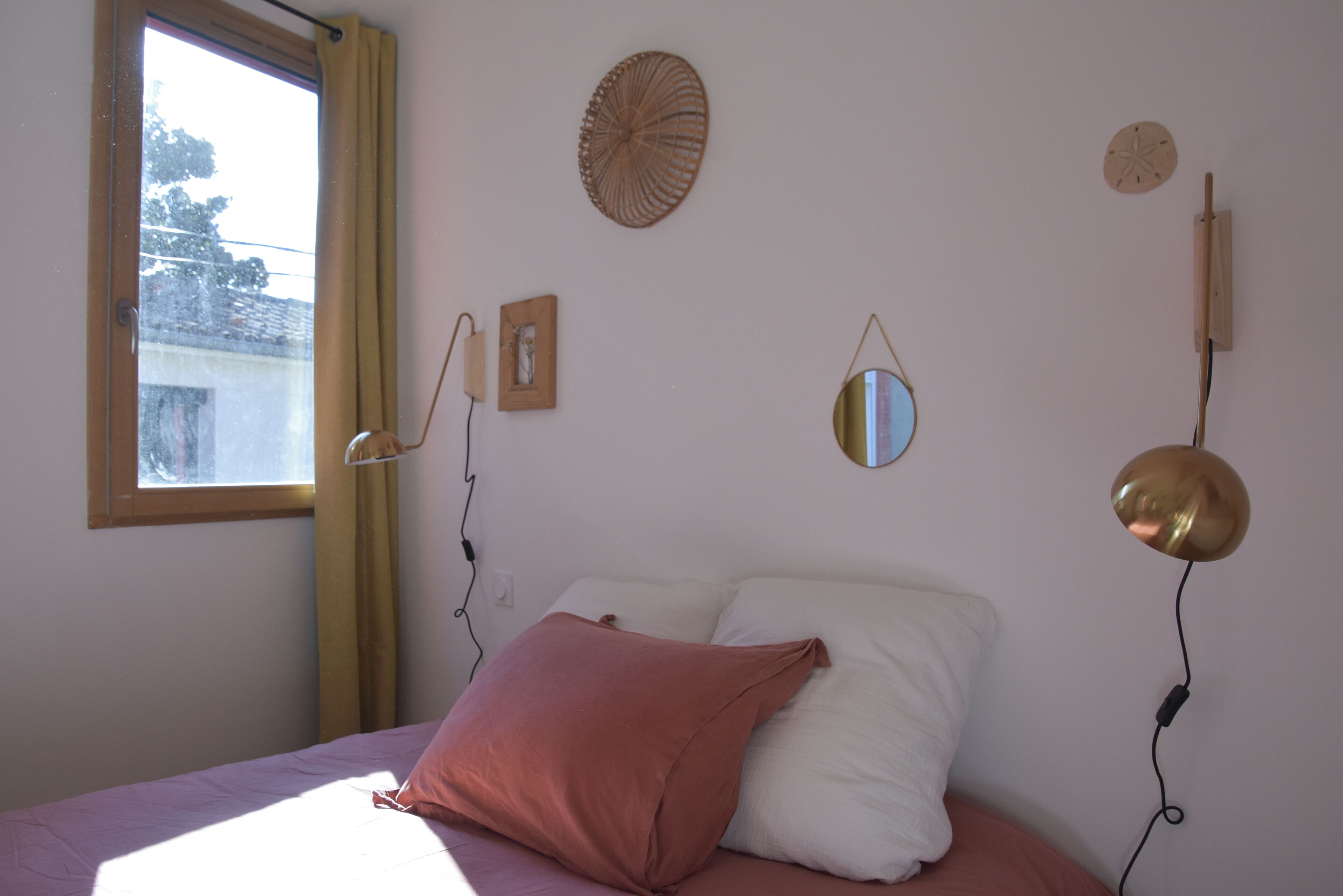 A bedroom with a bed, a window, and wall decorations including a mirror and a wall clock.