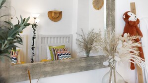 Ein Schlafzimmer mit einem Bett, einem Spiegel, einer Lampe, einer Stoffaffe und einer Vase mit Trockenpflanzen.