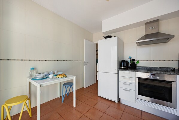 A compact kitchen with a white refrigerator, oven, and a small dining table with stools. - Villa 'V-Blue' with Private Pool, Wi-Fi and Air Conditioning (Alvor)