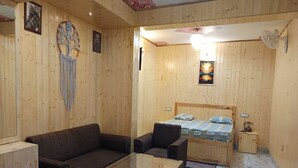 Ein gemütliches Zimmer mit Holzvertäfelung, einem Bett mit gemustertem Überwurf, einem dunkelbraunen Sofa und einem kleinen Tisch.