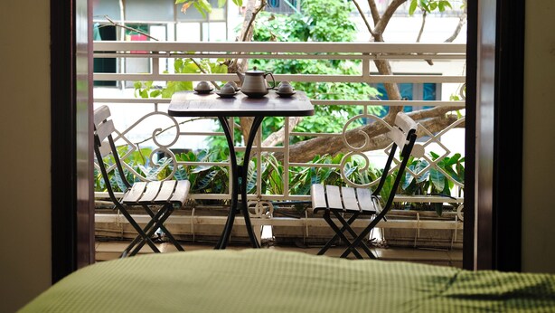 A balcony with a table set for tea, two chairs, and a view of greenery and buildings. - Seréne - Old Quarter Centre Hotel Ha Noi (Hanoi)