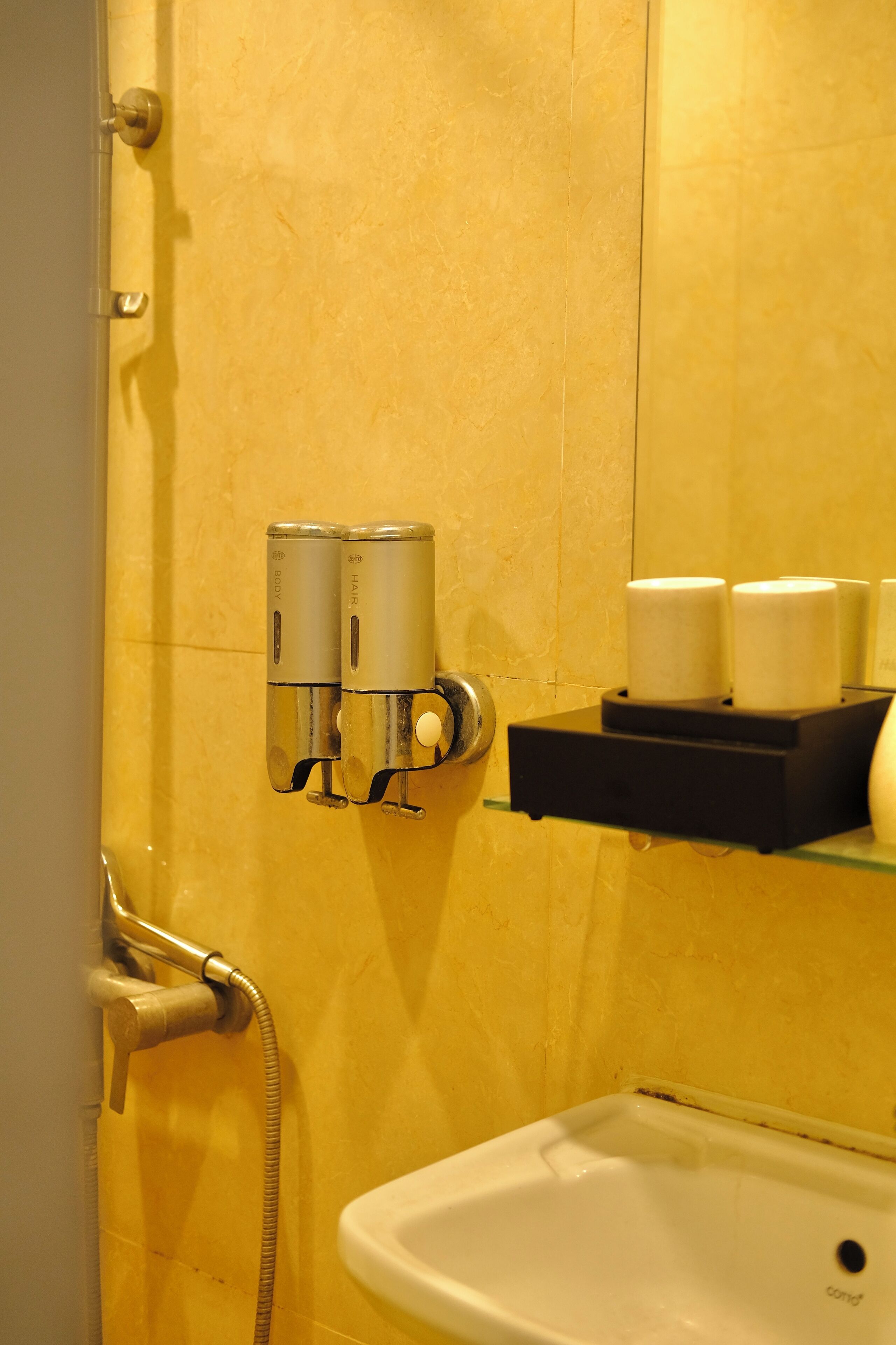 A bathroom with a yellow tiled wall, a white sink, and a towel dispenser.