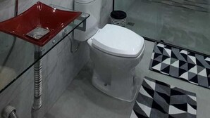 Une salle de bain moderne avec une douche à l’italienne en verre, un lavabo en verre rouge et des toilettes blanches.