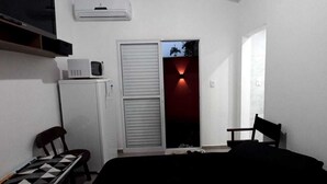 Une petite pièce, peu meublée, comprenant un lit, un bureau, une chaise, un four à micro-ondes et une armoire.