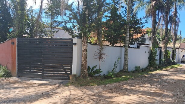 Une propriétéClose, entourée d’un mur blanc, avec une porte en bois et un chemin de terre menant à une maison dont le toit est recouvert de tuiles.