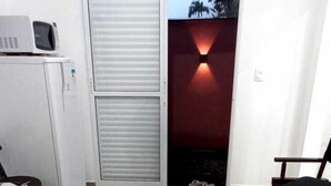Une chambre avec un lit, un bureau, un four à micro-ondes et une porte coulissante donnant sur un balcon avec un mur rouge et une vue sur des palmiers.