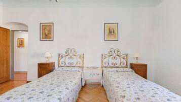 Une chambre avec deux lits, des têtes de lit en bois, une armoire en bois et une petite table de chevet avec une lampe.