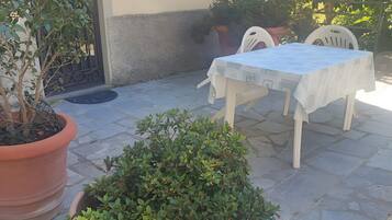 Eine Terrasse mit Tisch und Stühlen, Blumentöpfen und einem Hauseingang.