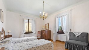 A bedroom with two beds, a bench, a dresser, a mirror, and a chandelier. - Casa Relax in the Countryside (Pomino)