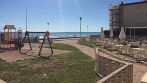 Une terrasse au bord de la plage avec des sièges extérieurs, un espace de jeux pour enfants et une vue sur l’océan.
