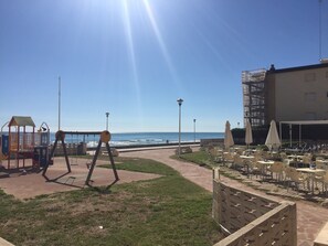 Eine Terrasse am Strand mit Sitzmöglichkeiten im Freien, einem Spielbereich für Kinder und Blick auf den Ozean.