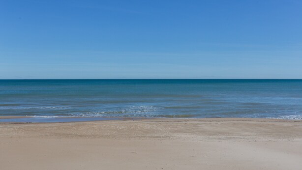 Une plage avec un ciel dégagé et une mer calme.