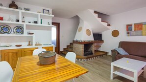 Un salon avec une table en bois, des chaises blanches, un canapé marron, une cheminée et un escalier.