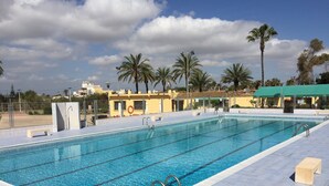 Une piscine à l’eau cristalline, entourée de palmiers et bordée d’un bâtiment doté d’un toit végétalisé.