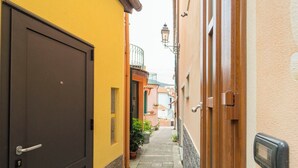 Une ruelle étroite, avec une porte fermée sur la gauche, une porte en bois sur la droite et un petit espace jardin agrémenté de plantes en pot.