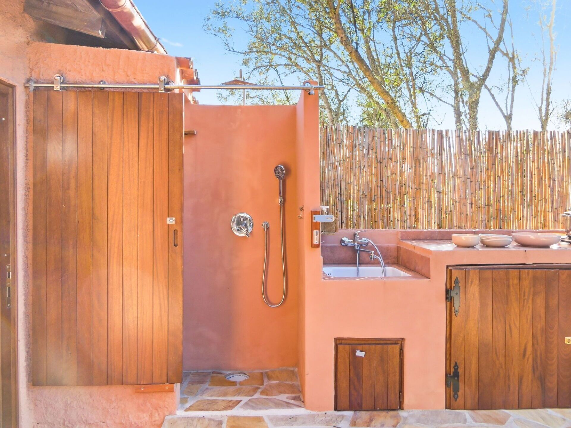 Una porta in legno che dà su un bagno con doccia, lavandino e un piccolo armadietto.