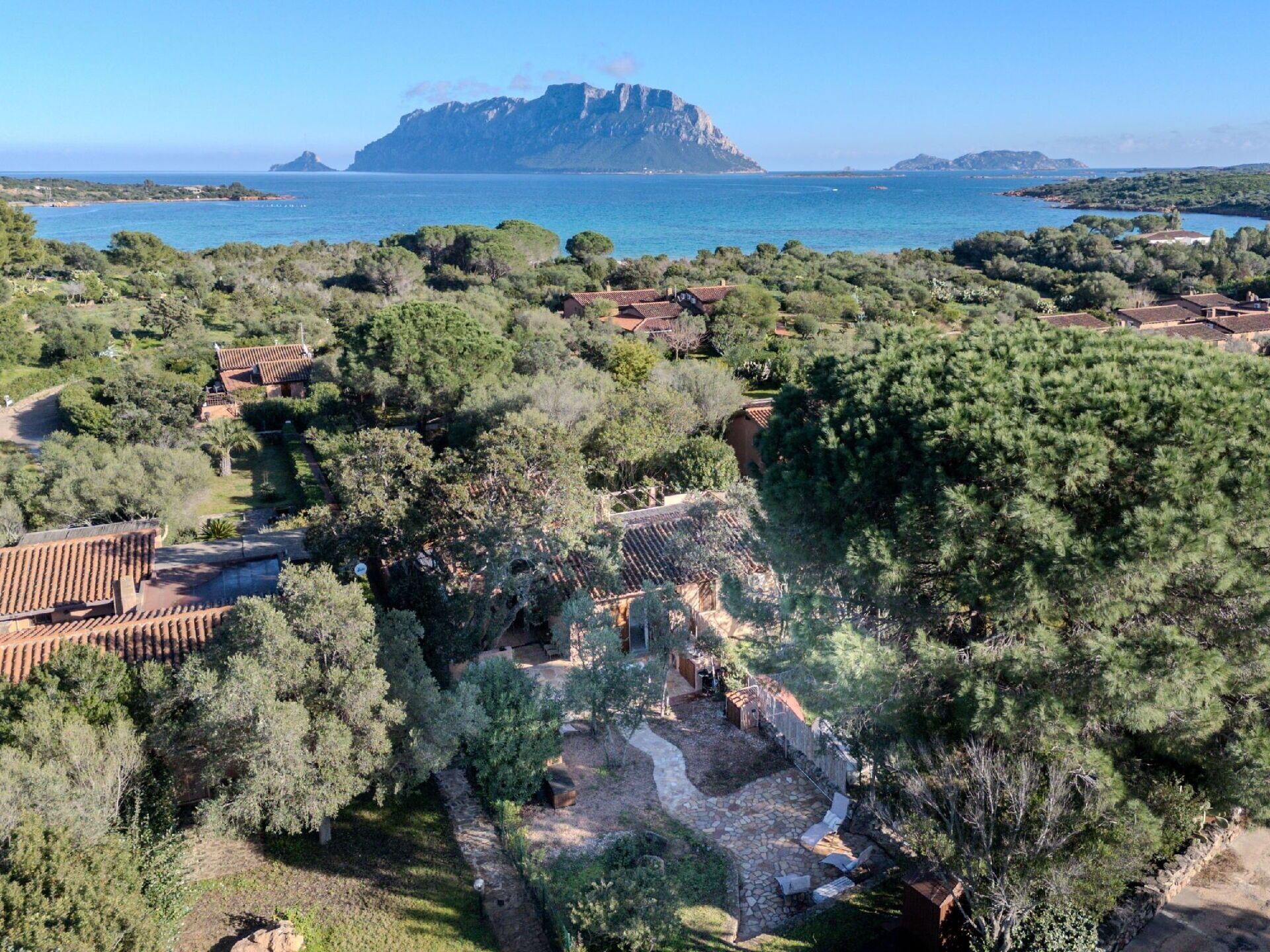 Een kustpand met terrassen, een pad van stenen en uitzicht op zee en een berg in de verte.