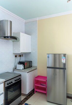 Una cocina con armarios blancos, un horno de acero inoxidable, un tostador, un refrigerador y una estantería rosa.