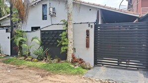Un edificio residencial con entrada protegida por un portón, una ventana pequeña y un equipo de aire acondicionado instalado en la pared.