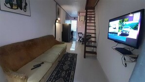 Una sala de estar con sofá, televisor, escalera y una puerta que da a otra habitación.