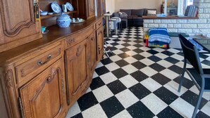 Een kamer met een houten kast met daarin verschillende serviezen, een zwart-wit schakeerd vloer, een bank en een stenen muur.