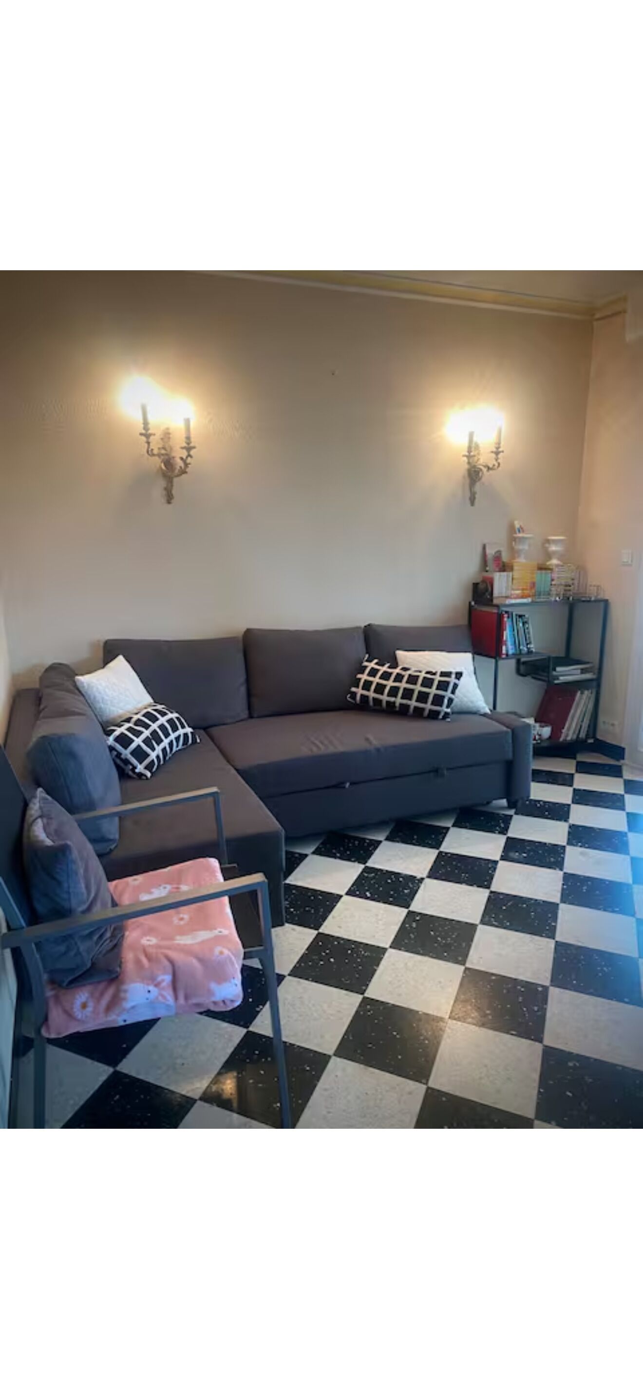 Un salon avec un sol à carreaux, un canapé, un fauteuil et une bibliothèque.