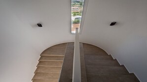 Een moderne trap met een golvend ontwerp, leidend naar een balkon met uitzicht op een heuvellandschap.