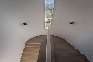 Eine moderne, geschwungene Treppe führt zu einem Balkon mit Blick auf eine hügelige Landschaft.