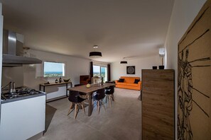 Eine moderne Küche mit Essbereich, Blick durch das Fenster und einem orangefarbenen Sofa im Wohnzimmer.
