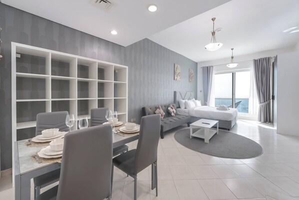 Una sala de estar moderna con comedor, sofás grises, una mesa de centro blanca y un amplio ventanal con cortinas.