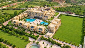 A large hotel with multiple swimming pools, a well-maintained lawn, and a mountainous backdrop. - The Surya Golden Palace Pushkar (Pushkar)